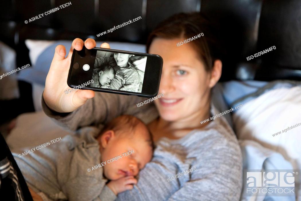 Stock Photo: Baby girl sleeping on mother's chest, while mother takes self portrait of them both, using smartphone.