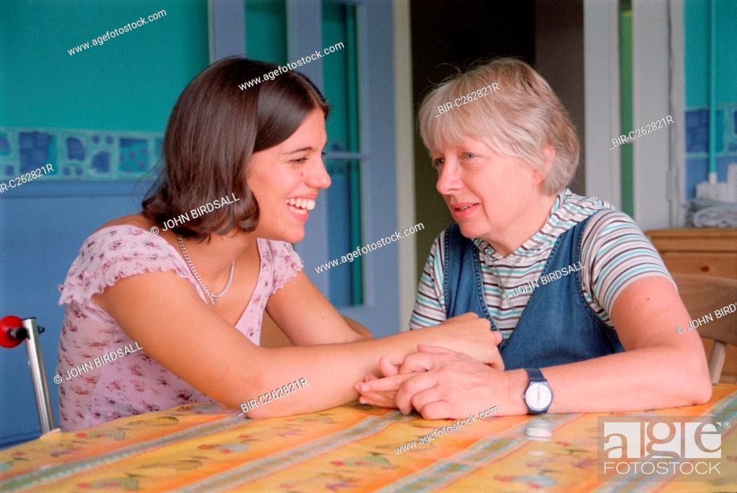 Stock Photo: Teenage girl with physical disability sitting at kitchen table in residential respite care home laughing and holding hands with carer,.
