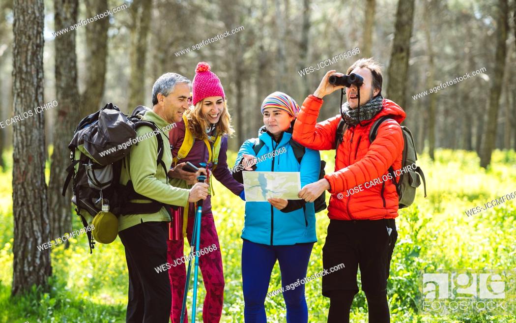 Stock Photo: Man looking through binoculars standing by friends sharing map in forest.