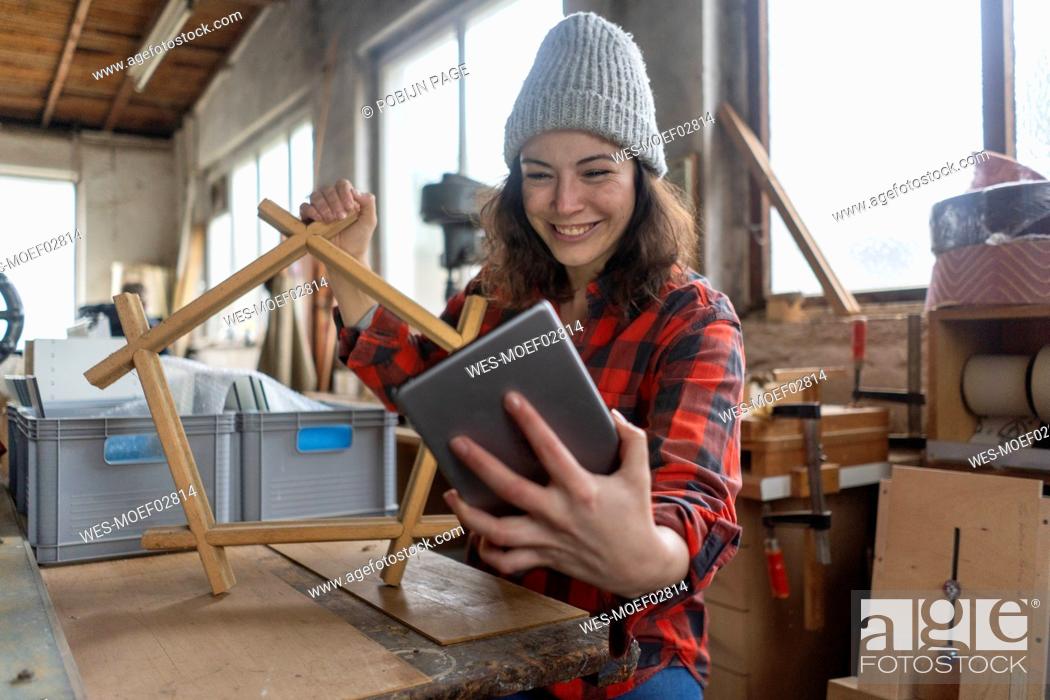Stock Photo: Smiling carpenter holding tablet and workpiece in her workshop.