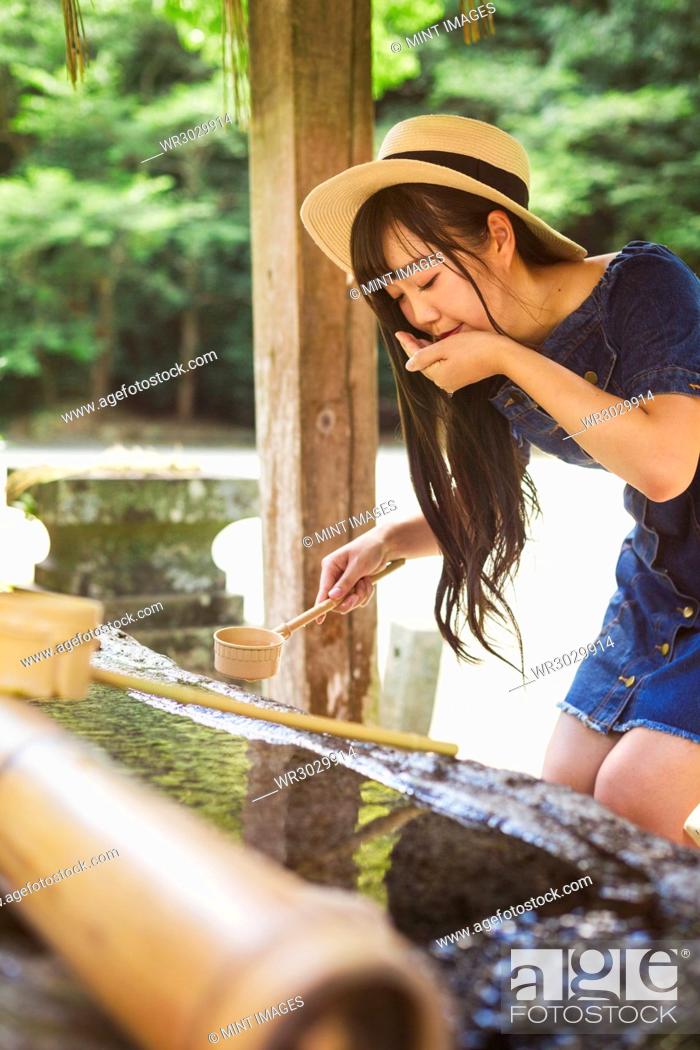 Stock Photo: Young woman wearing blue dress and hat using bamboo water hand washing basins at Shinto Sakurai Shrine, Fukuoka, Japan.