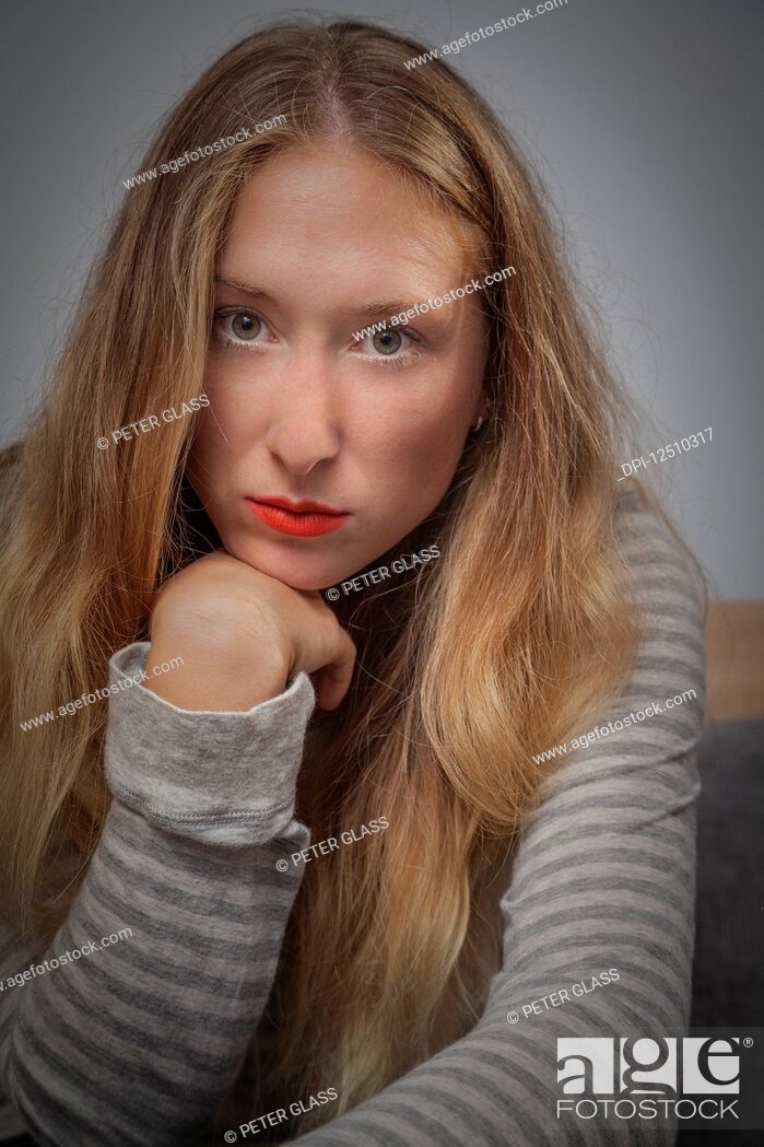 Stock Photo: Young woman with long blond hair posing for the camera while resting her chin on her hand; Connecticut, United States of America.