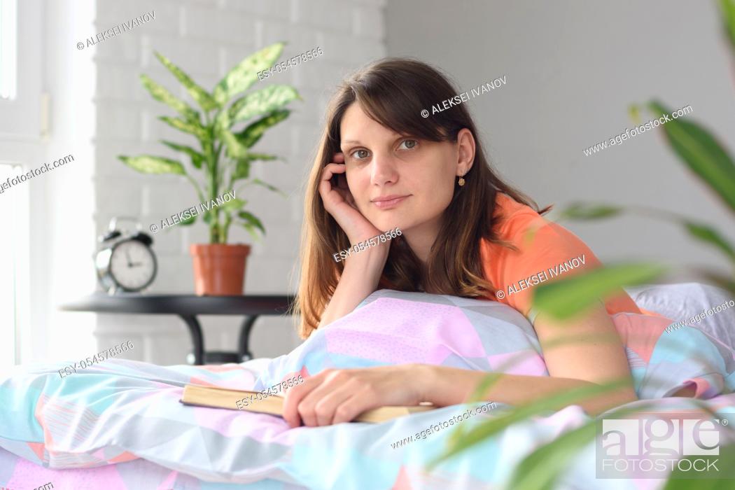 Stock Photo: The girl at home in bed reads a book and looked distracted.
