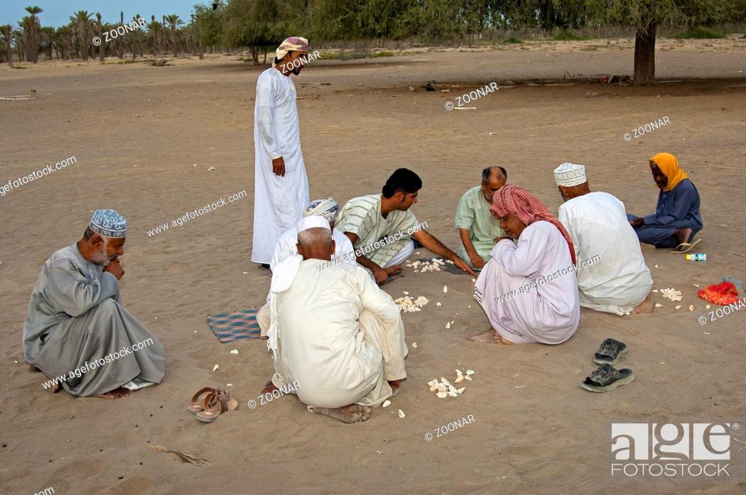 Stock Photo: Eine Gruppe omanische Männer spielt Hawalis mit Muscheln im Sand, omanische Variante des Mancala-Spiels, Sultanat Oman / A group of Omani men playing Hawalis.