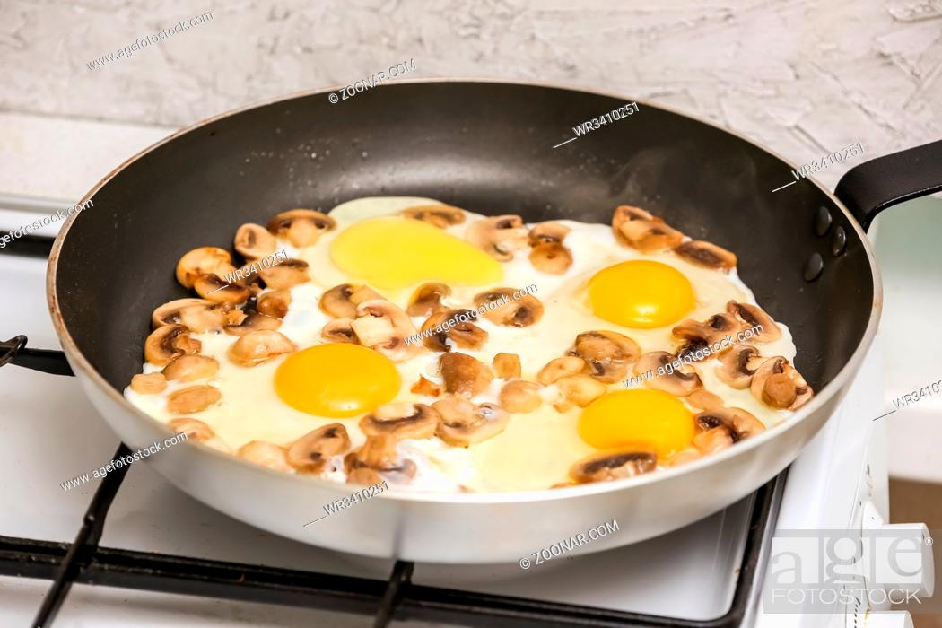 Photo de stock: Fried mushrooms champignons and fried eggs in a frying pan on gas stove.