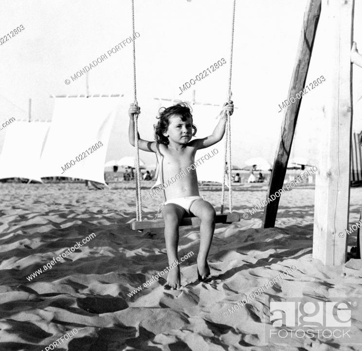 Stock Photo: Little girl Lidia Ciani, who won Miss Cesenatico for kids, having fun on a seesaw at the beach. Bellaria, 1953.