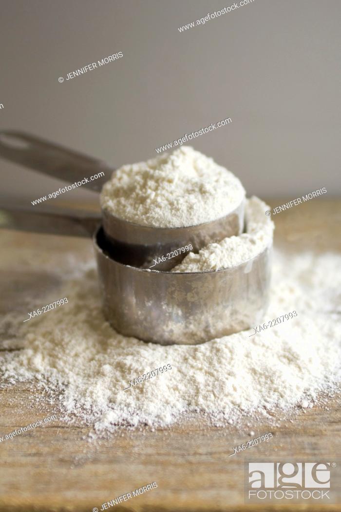 Stock Photo: Two measuring cups full of flour sit on a wooden board.