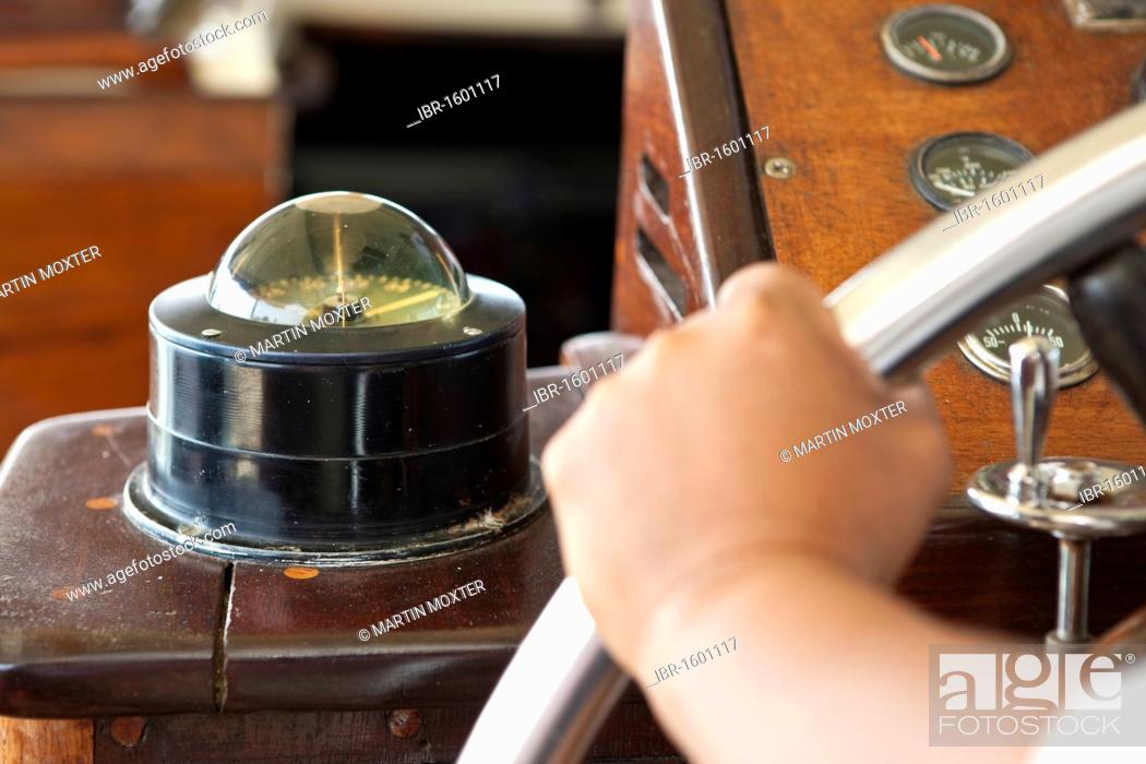 Stock Photo: Frimly gripped steering wheel of a wooden boat, the compass at back.