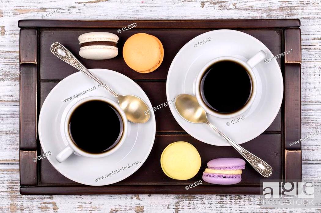 Stock Photo: Two cups of coffee, spoon and macaron cakes on tray on white wooden table. Lifestyle concept. Close up. Top view.