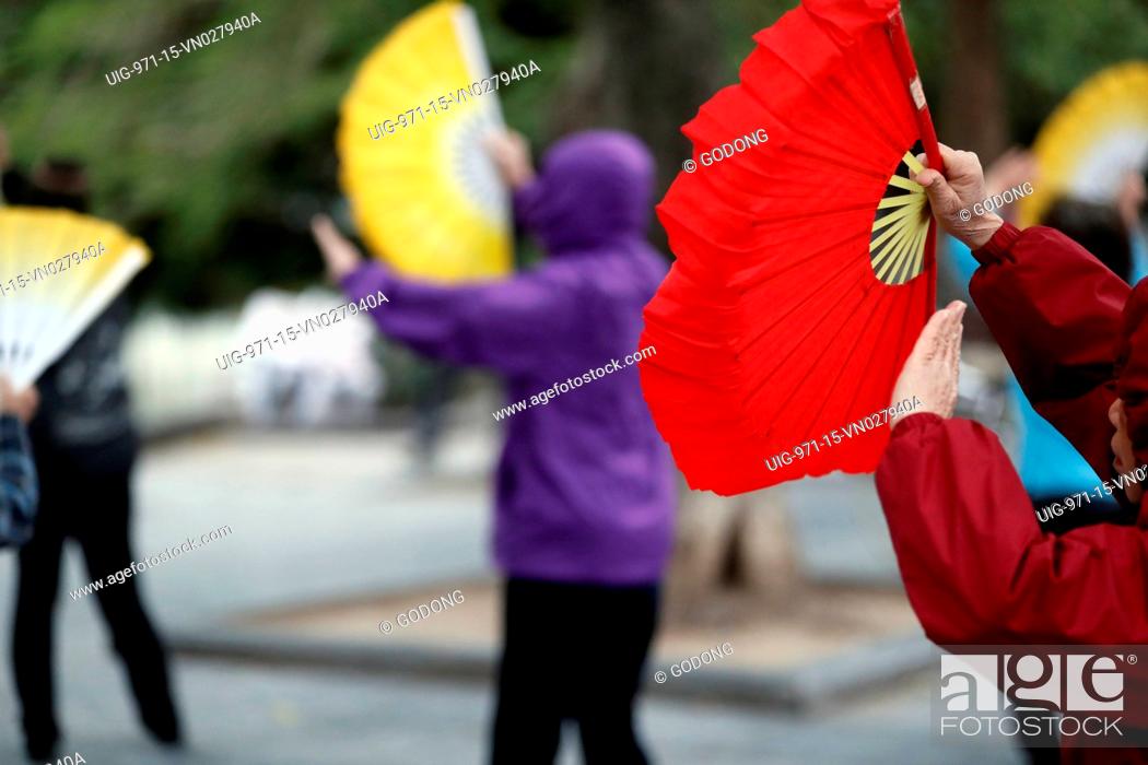 Stock Photo: Early morning tai chi session along the banks of Hoan Kiem lake. Exercises with fans.