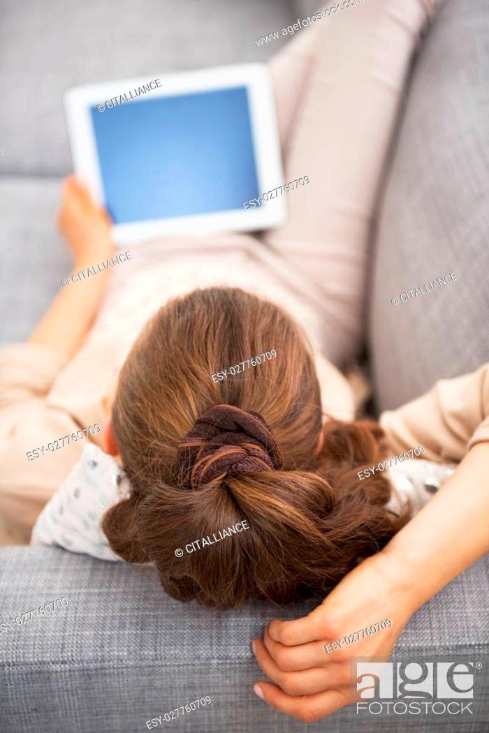 Stock Photo: Young woman laying on sofa with tablet pc . rear view.