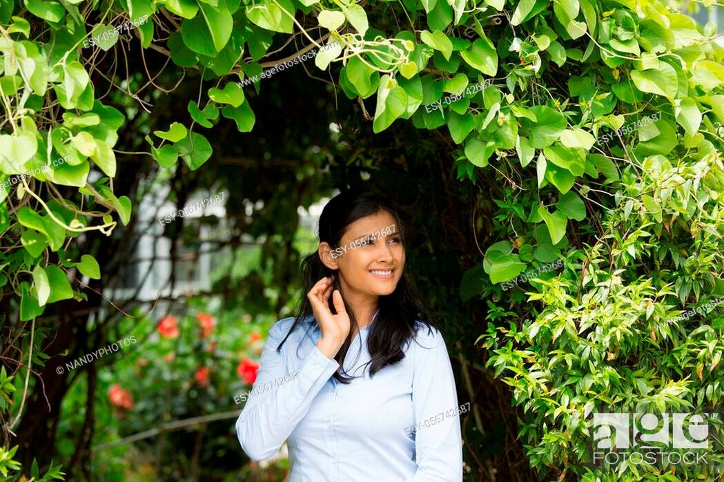 Stock Photo: Closeup portrait of confident smiling happy pretty young woman in blue shirt enjoying a fresh new day, isolated background of green shrubs and flowers.