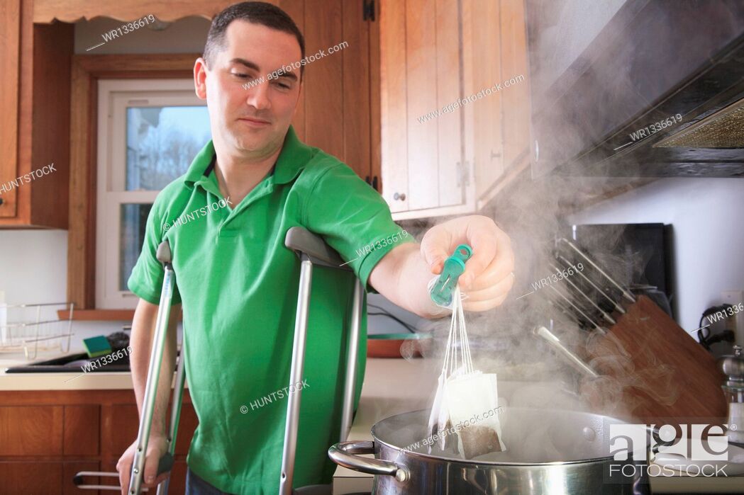 Stock Photo: Man after anterior cruciate ligament (ACL) surgery with crutches making tea in the kitchen.
