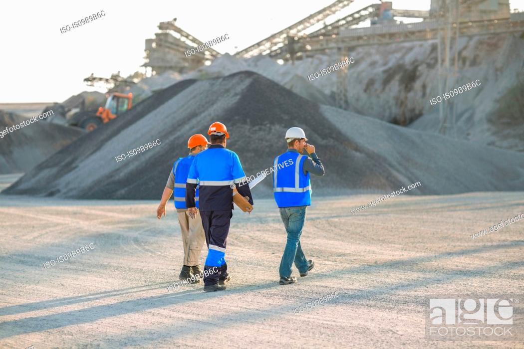 Stock Photo: Three quarry workers, walking across quarry, rear view.