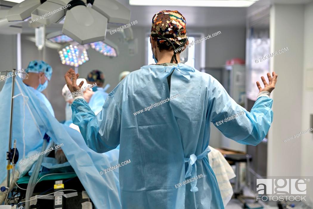 Stock Photo: Surgeon stands in the operating room on the background of the surgery. He wears a colorful hat with medical clothes. Horizontal.