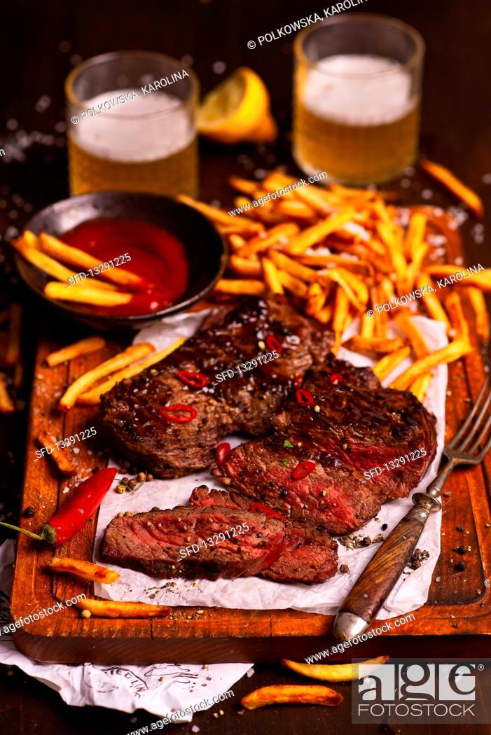 Photo de stock: Beef steak in a sticky sauce with fries, ketchup and beer.