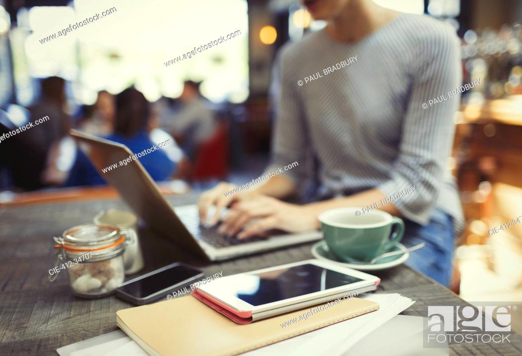 Stock Photo: Creative businesswoman working at laptop behind digital tablet in cafe.