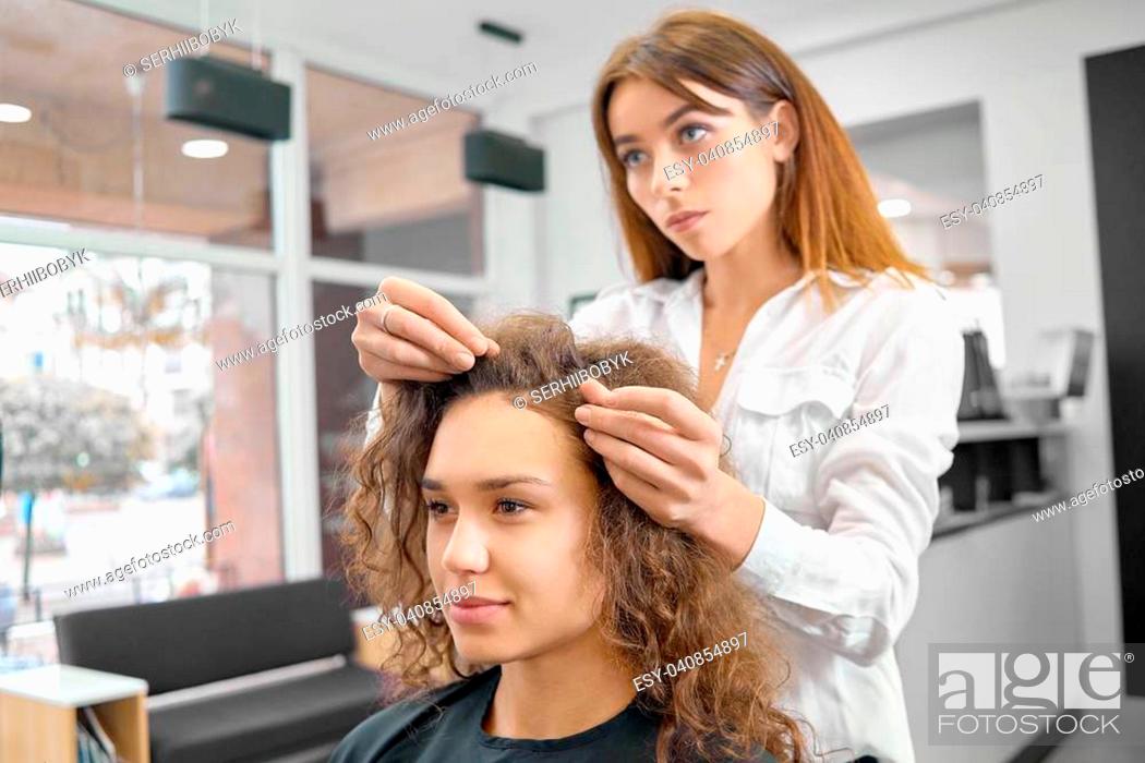 Stock Photo: Doing new hairstyle in beaty salon with professional hairstyler. Young model having brown curly hair, pretty smile, dark eyes, looking forward.