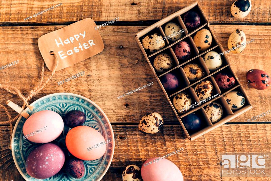 Stock Photo: Easter decor. Top view of colored Easter eggs on plate and Easter quail eggs in box lying on wooden rustic table.