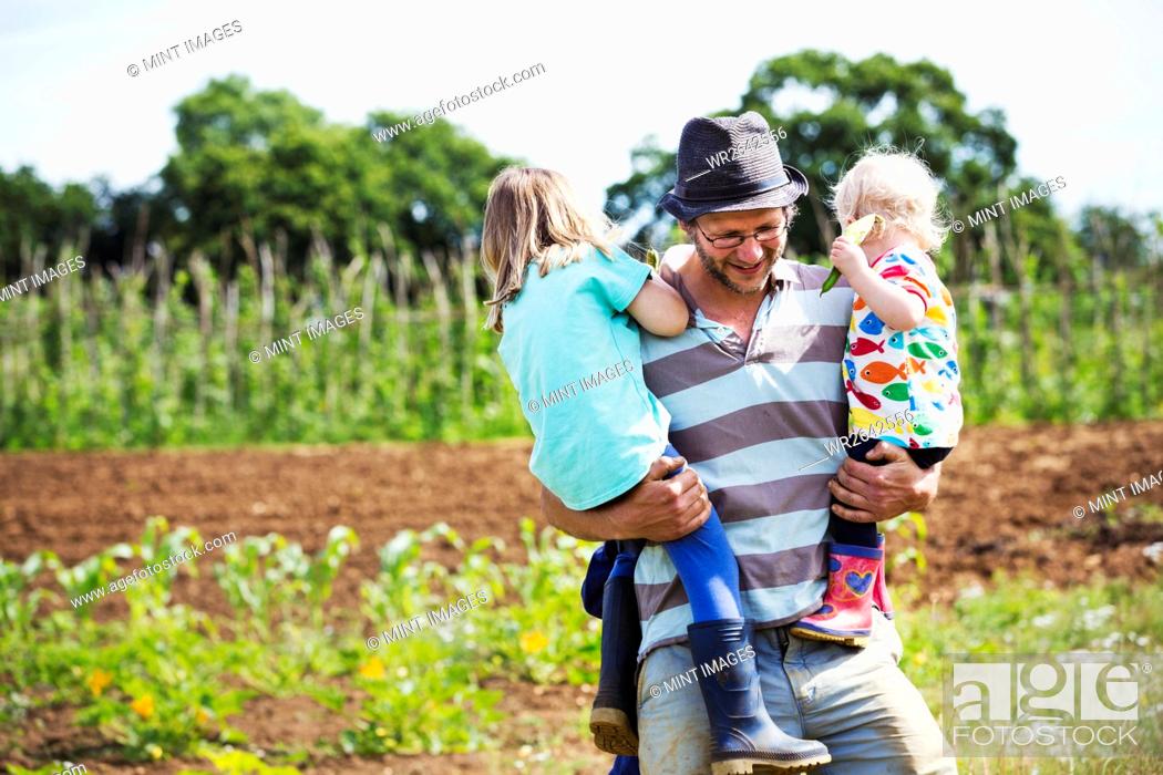 Stock Photo: A man carrying two children in a field.