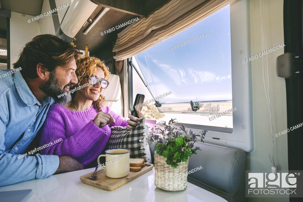 Photo de stock: Tourist young adult people enjoy phone connection and freedom sitting inside a modern camper van and enjoying beach outside.