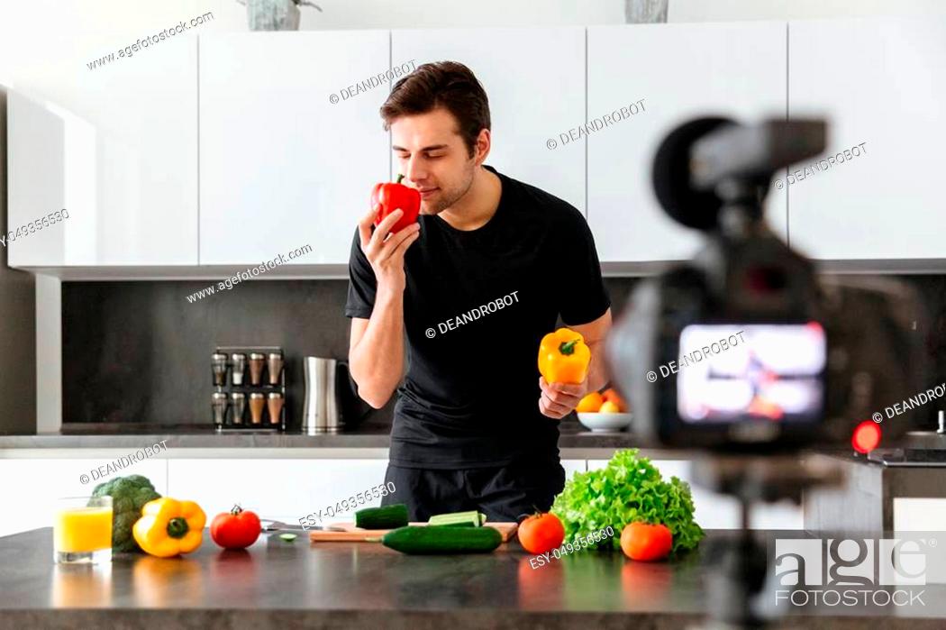Stock Photo: Attractive young man filming his video blog episode about healthy food cooking while standing at the kitchen.