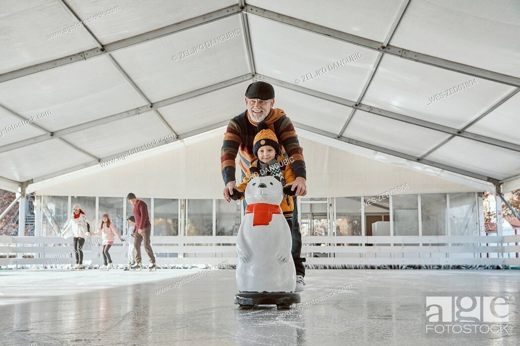 Stock Photo: Grandfather and grandson on the ice rink, ice skating, using ice bear figure as prop.