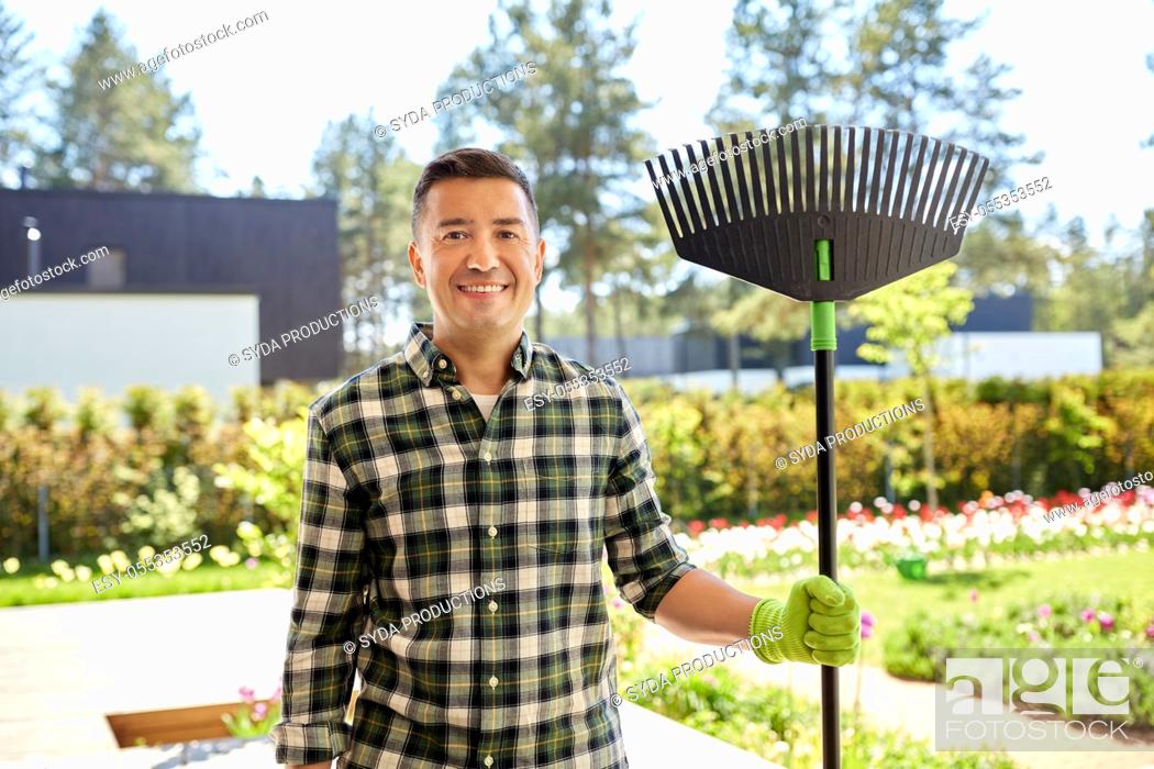 Stock Photo: happy middle-aged man with leaf rake at garden.