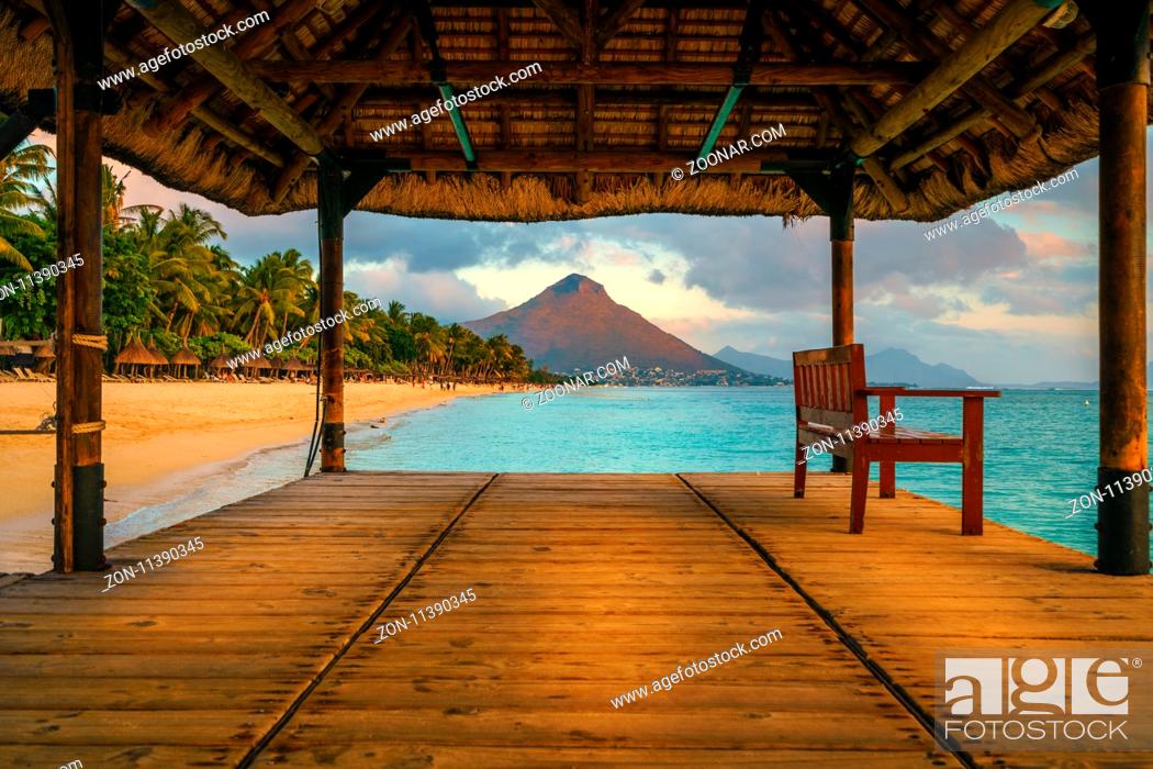 Stock Photo: Wonderful view across the pier, on the left the tropical beach and in the background a beautiful mountain illuminated by red during sunset, Mauritius.
