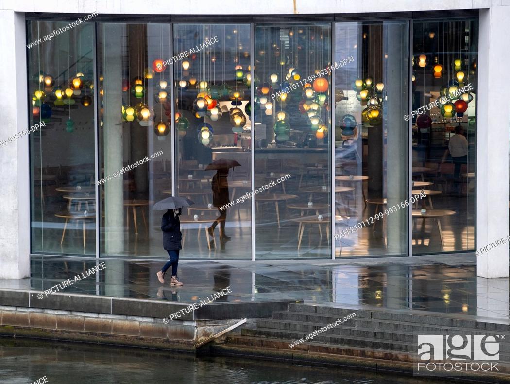 Stock Photo: 12 January 2021, Berlin: A woman walks past the Bundestag restaurant on the banks of the Spree river, where tables without chairs are standing around.