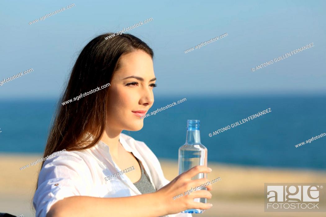 Stock Photo: Portrait of a serious woman holding a water bottle sitting on a bench on the beach.