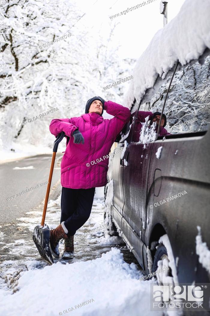 Stock Photo: Contemplative man with snow shovel leaning on car.