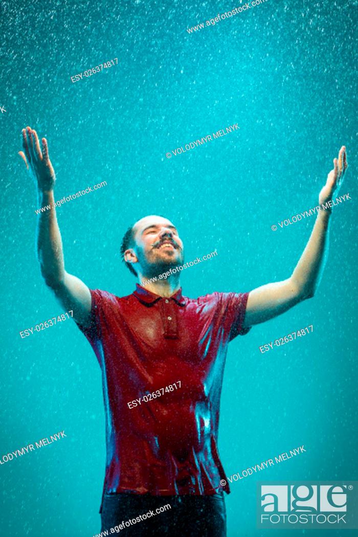 Stock Photo: The portrait of young man in the rain.The man smiling on a turquoise background.