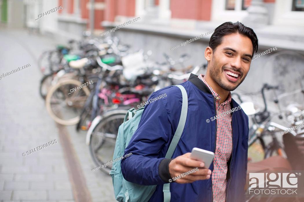 Stock Photo: Portrait enthusiastic young man with cell phone at bike rack on city street.