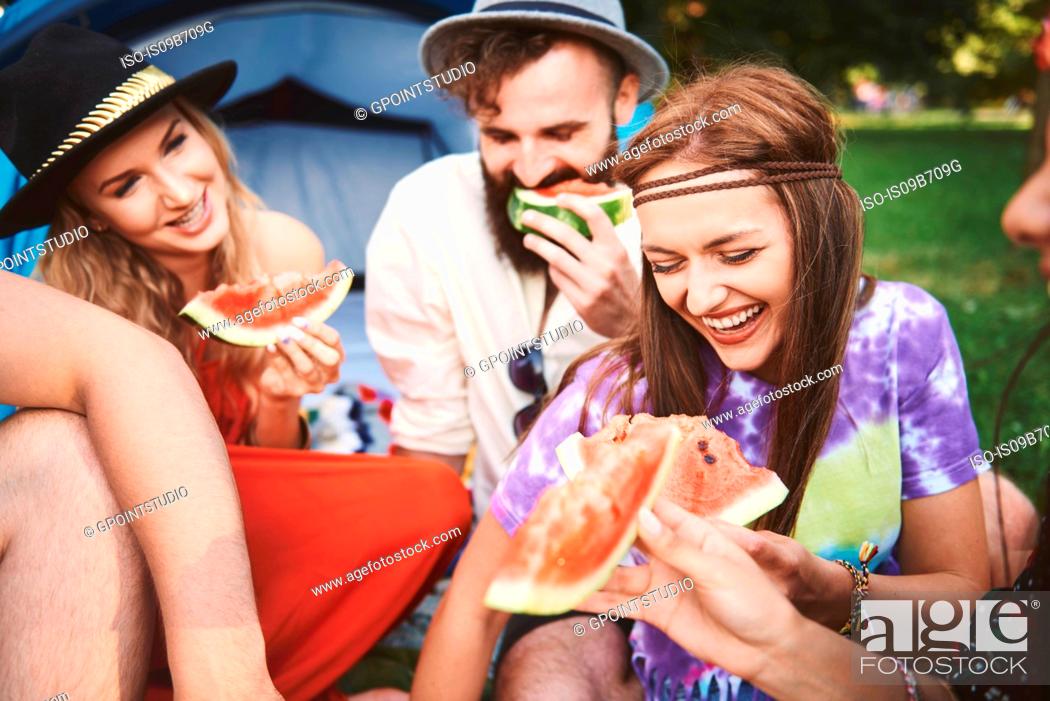 Stock Photo: Young boho adult friends eating melon slices at festival.