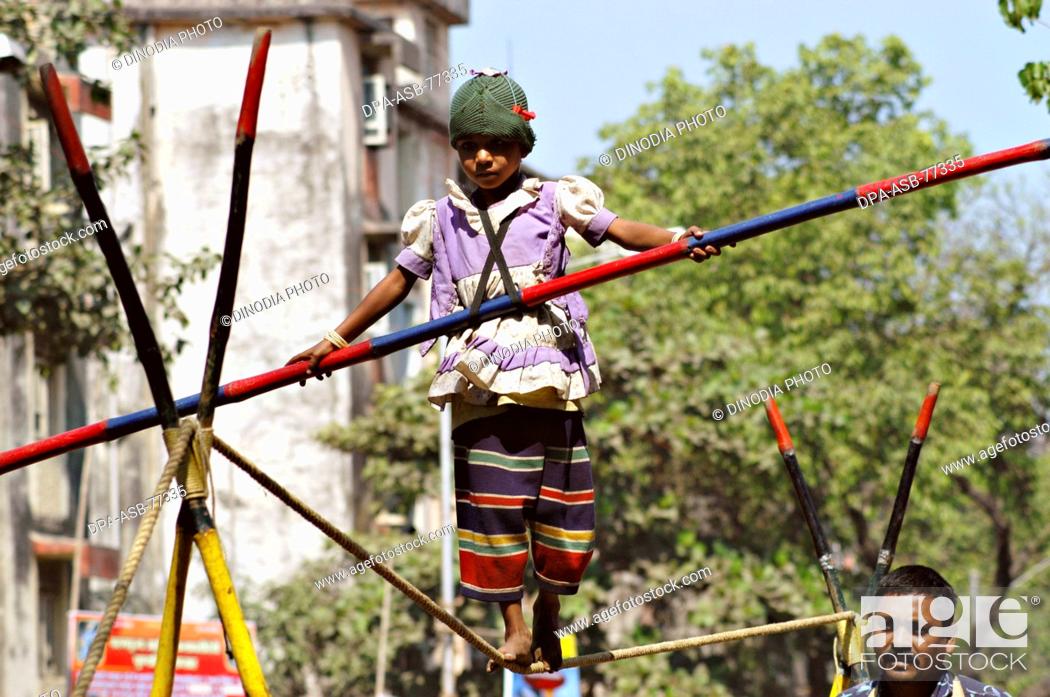 Stock Photo: South Asian girl working street performer balancing act by walking on rope with bamboo in hand ; after  performance ; parents of the child collect money from.