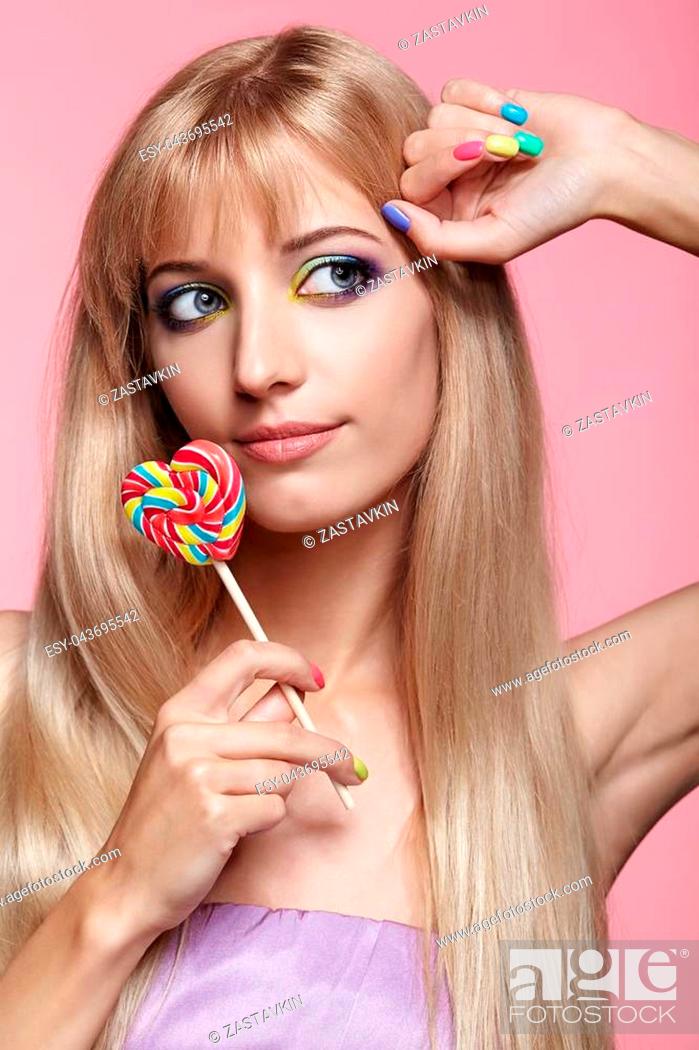 Stock Photo: Beauty portrait of young blonde woman on pink background. Female with candy lollipop on stick in hands. Girl has finger nails with bright yellow, green.