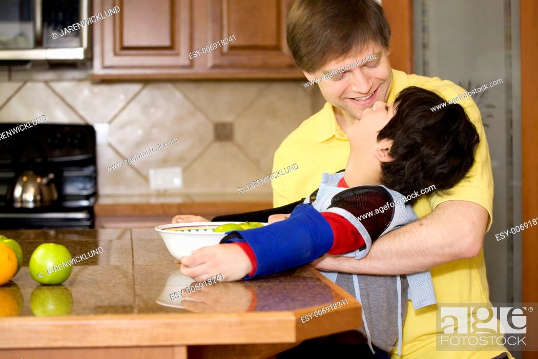 Stock Photo: Father helping disabled son putting fruit into bowl in the kitchen. Son has cerebral palsy.