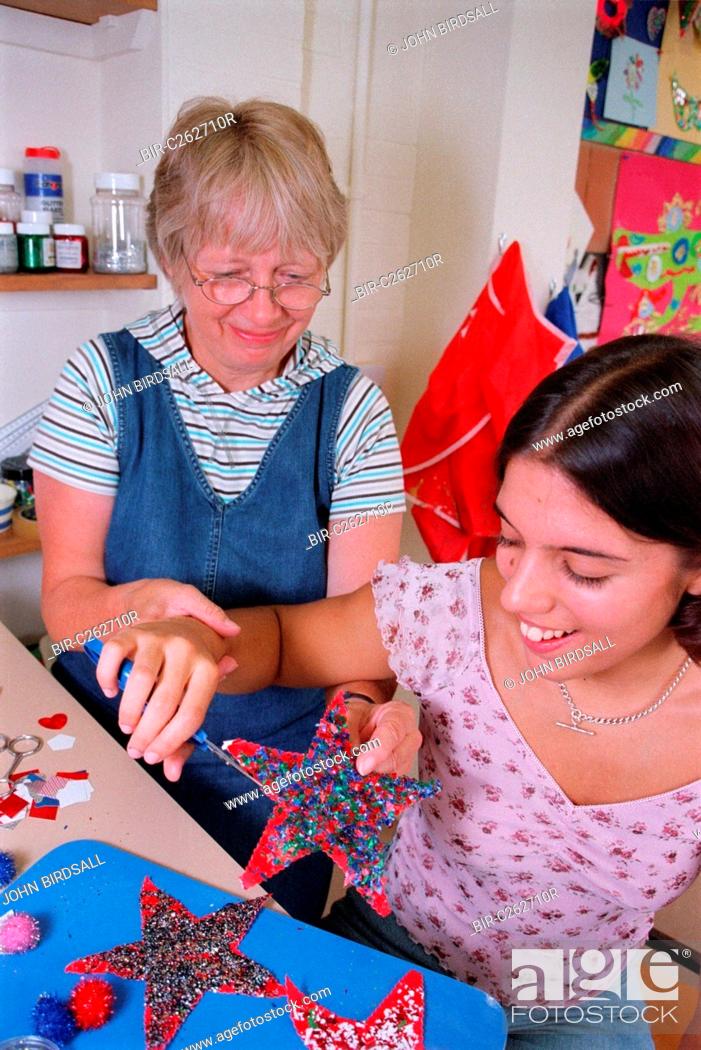 Stock Photo: Carer assisting teenage girl to use self opening scissors in residential respite care home,.