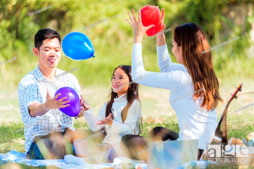 Stock Photo: Happy Asian young family father, mother and child little girl having fun and enjoying outdoor sitting on picnic blanket playing balloons at summer garden spring.