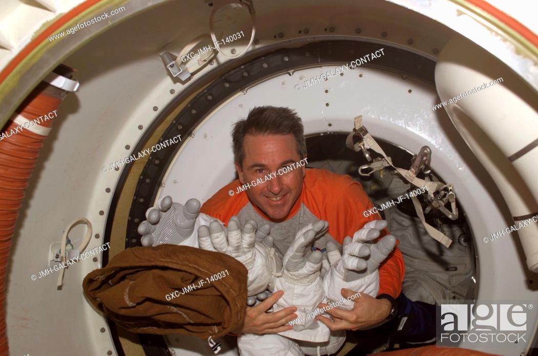 Stock Photo: Astronaut Stephen K. Robinson, STS-114 mission specialist, holds Extravehicular Mobility Unit (EMU) spacesuit gloves as he floats through a hatch while Space.