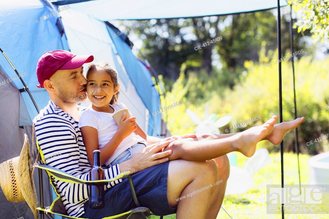 Imagen: Happy, affectionate father holding daughter in lap at sunny campsite.