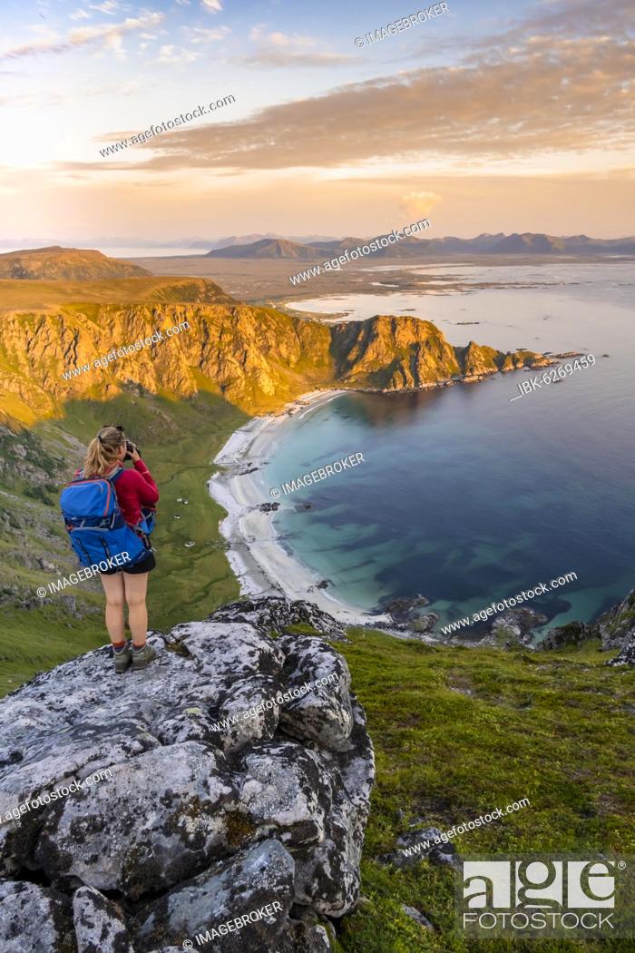 Stock Photo: Hiker standing on a rocky outcrop overlooking beach and sea, summit of Måtinden mountain, near Stave, Nordland, Norway, Europe.