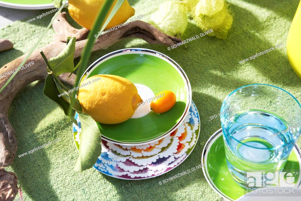 Stock Photo: A lemon and a kumquat in a green bowl next to a water glass.