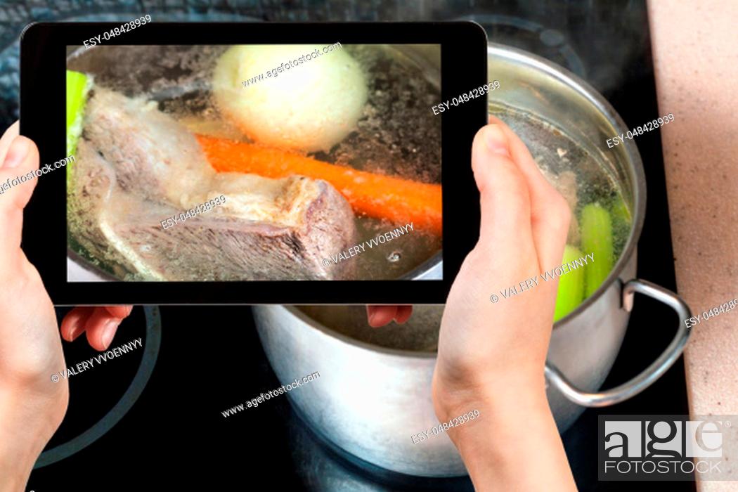 Stock Photo: travel concept - visitor photographs of cooking soup with boiling beef broth in steel stewpan close up on caramic stove on smartphone.