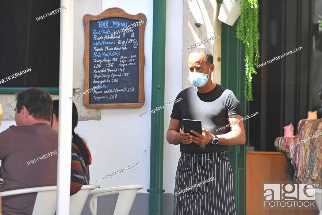 Stock Photo: A waiter with face mask, mask waits for guests in front of the restaurant, gastronomy. In Portugal, the tourism industry is suffering massively from the.