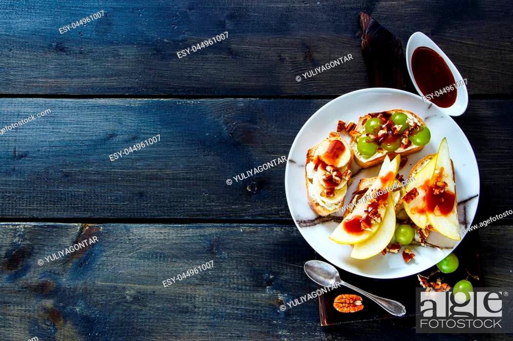 Stock Photo: Homemade crostini with pear, cream-cheese, grapes, banana, nuts and chocolate caramel. Breakfast toasts or snack sandwiches on vintage chopping board over.