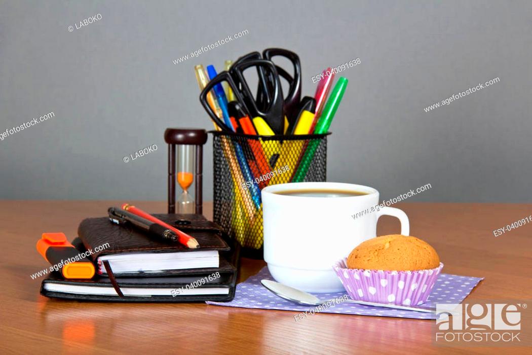 Stock Photo: A office supply in a support hourglasses, a cup of coffee a spoon a napkin and cake on a table.