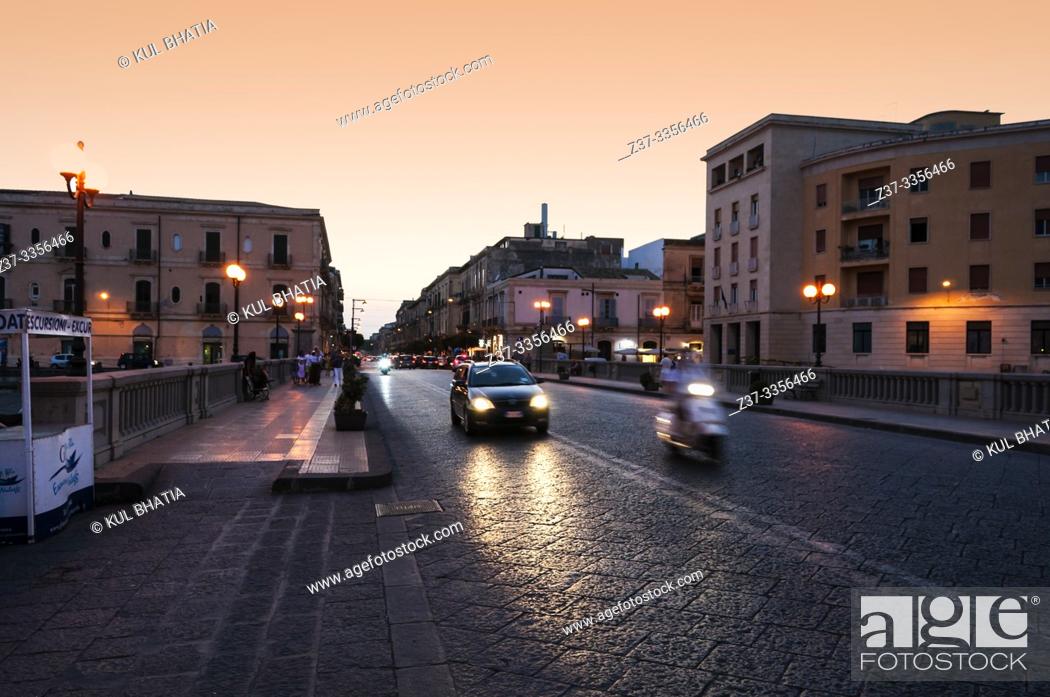 Stock Photo: Vittorio Emmanuel bridge, connecting Ortigia and Siracusa at dusk. Dark stones in the pavement glow in the headlights of cars and scooters on a warm summer.