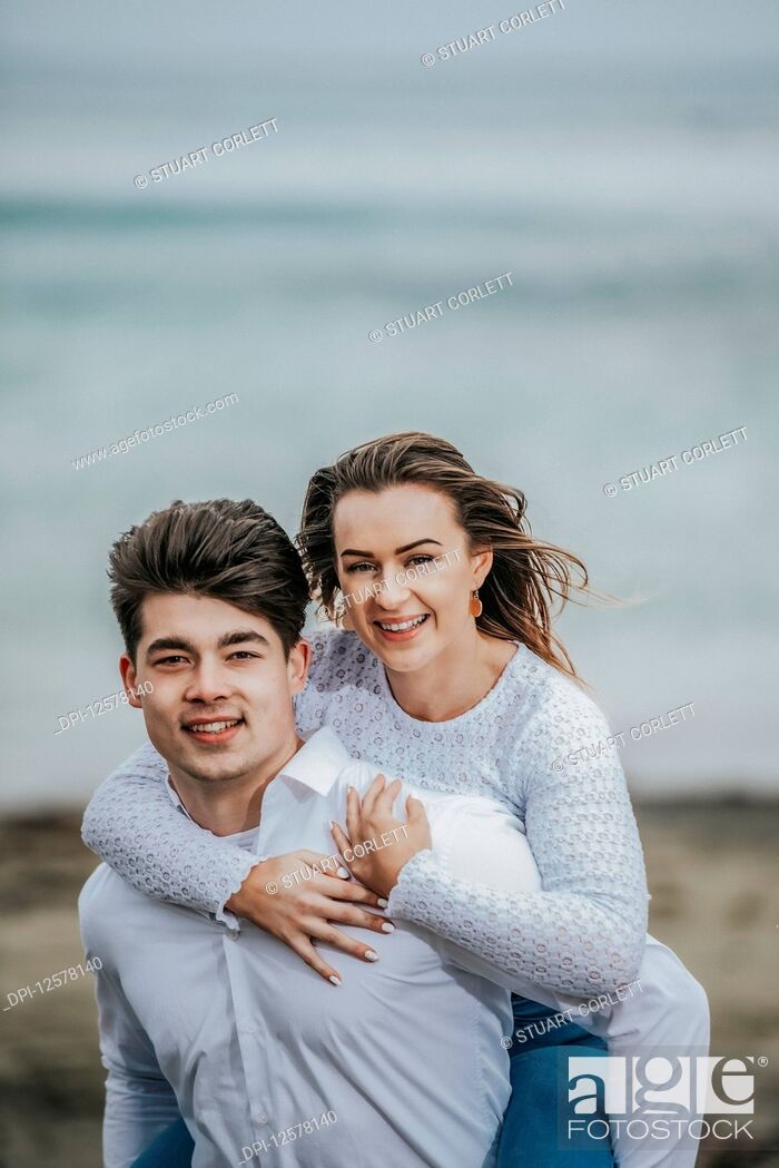 Stock Photo: Portrait of a young couple at the beach, the young woman being carried on the young man's back; Wellington, North Island, New Zealand.